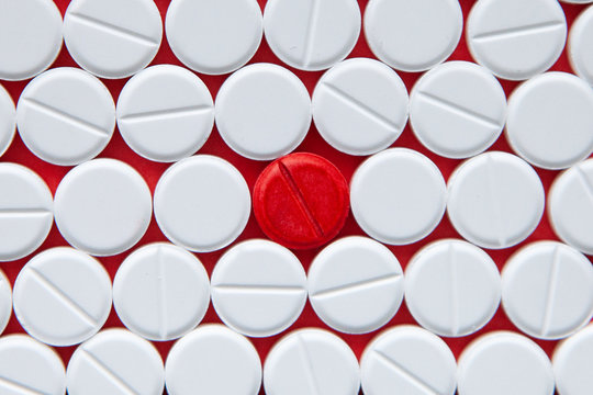 Top view of a pile of white medicine pills on a white surface. One tablet of red medication. Vaccine concept