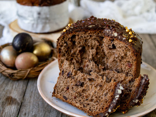 Amazing Chocolate Easter Cake with chocolate drops and dry cherries on an old wooden background with black and golden eggs. Slice of cake. Easter concept. Selective focus, close up.