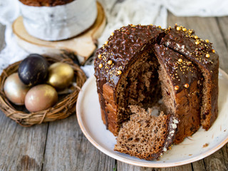 Amazing Chocolate Easter Cake with chocolate drops and dry cherries on an old wooden background with black and golden eggs. Slice of cake. Easter concept. Selective focus, close up.