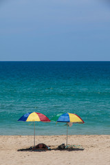 A tourist sleep under two colorful umbrellas on white sand beach.