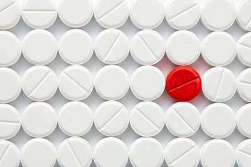 Top view of a pile of white medicine pills on a white surface. One tablet of red medication. Vaccine concept