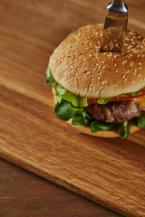 knife in delicious meat burger with cheese, greenery and tomatoes and sesame
