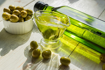 glass sauceboat with extra virgin olive oil,  fresh green olives and bottle on wooden table.