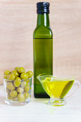 glass sauceboat with extra virgin olive oilб  fresh green olives and bottle on wooden table.