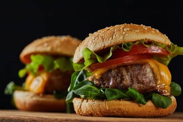 selective focus of delicious meat burgers with cheese and vegetables on wooden chopping board...