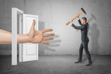 Businessman with axe in hands on the right ready to hit huge human hand reaching out through white doorway on the left. - obrazy, fototapety, plakaty