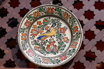 Traditional handmade ceramic plate displayed on a wooden surface, in direct sunlight, Romanian decorative object