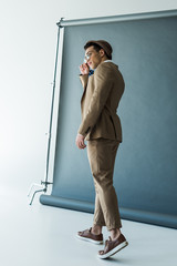 fashionable mixed race man in suit and hat posing on grey