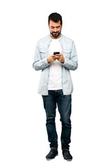 Full-length shot of Handsome man with beard sending a message with the mobile over isolated white...