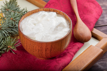 Close-up wooden bowl with yogurt, spoon and fir twig on red napkin  on wooden table.
