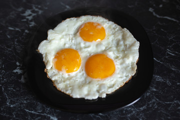 Breakfast. Fried eggs in a black plate on a dark background