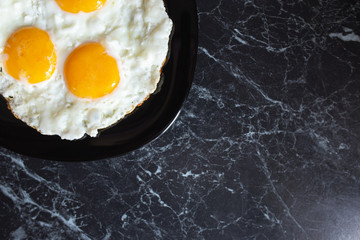 Breakfast. Fried eggs in a black plate on a dark background