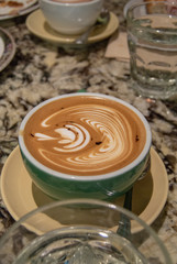 Hot cappuccino coffee with a beautiful leaf shape latte art in the ceramic cup on the marble top table.