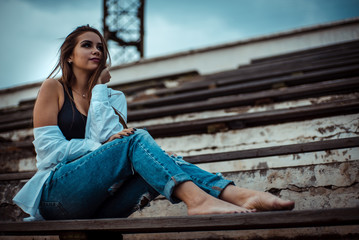 Attractive woman sitting with bare feet in the stadium. She's wearing a shirt and jeans