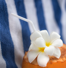 Coconut with Plumeria flowers and a drinking tube lying on a striped towel at a tropical resort