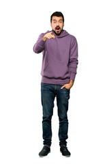 Full-length shot of Handsome man with sweatshirt surprised and pointing front over isolated white background