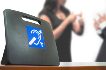 Two deaf people using American Sign Language next to a Tele Coil Magnetic Loop with T-switch with induction system for hearing aids. Empty copy space for Editor's text.