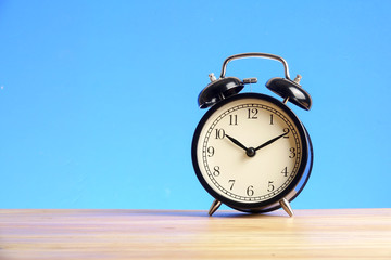 Black alarm clock on the wooden surface against the blue background.