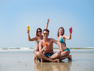 Two girls and a man on the beach drinking juice from glass glasses
