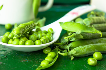 green peeled peas pods  in a spoon on a green background.