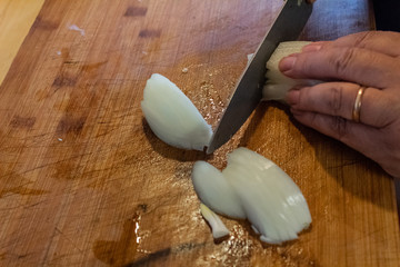 hands cut white onion with a knife with green rubber handle. On top of a wooden table kitchen, with food in it brands 