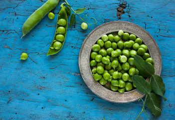 green peeled peas pods  in a spoon on a green background.