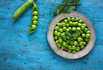 green peeled peas pods  in a spoon on a green background.