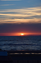 Sunset over the Ocean - View of the red sun sinking into the horizon and waves washing over the...