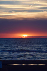 Sunset over the Ocean - View of the red sun sinking into the horizon and waves washing over the...