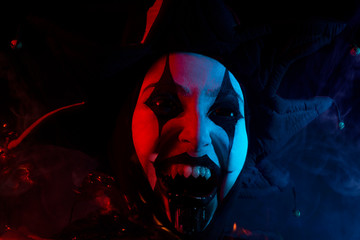 Creepy screaming jester's face with black eyes and fangs, close-up.