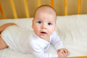 Cute little baby boy baby 4 months in white clothes lying on his stomach in his crib. Colic in baby. Health and childhood concept.