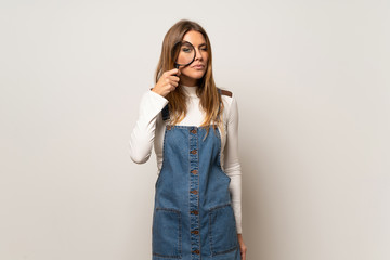 Beautiful woman over isolated white wall taking a magnifying glass and looking through it