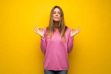 Woman with pink sweater over yellow wall in zen pose