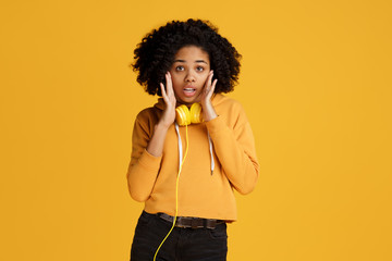 Shocked african american young woman dressed in casual clothes and headphones over yellow...