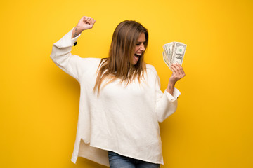Blonde woman over yellow wall taking a lot of money