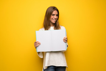 Blonde woman over yellow wall holding an empty placard for insert a concept