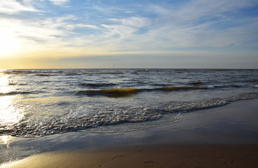 Sunset over the Ocean - View of the red sun sinking into the horizon and waves washing over the sand of the beach