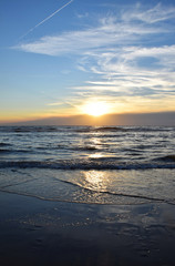Sunset over the Ocean - View of the red sun sinking into the horizon and waves washing over the sand of the beach
