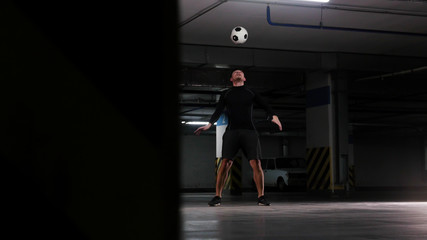Fototapeta na wymiar Underground parking lot. A soccer man training his football skills. Catching the ball on his forehead
