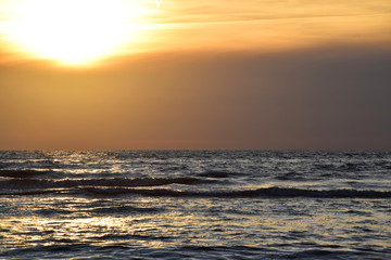 Sunset over the Ocean - View of the red sun sinking into the horizon and waves washing over the sand of the beach