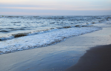 Sunset over the Ocean - View of the red sun sinking into the horizon and waves washing over the sand of the beach