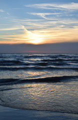 Sunset over the Ocean - View of the red sun sinking into the horizon and waves washing over the sand of the beach