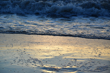 Sunset over the Ocean - View of the red sun sinking into the horizon and waves washing over the sand of the beach