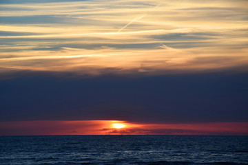 Obraz premium Sunset over the Ocean - View of the red sun sinking into the horizon and waves washing over the sand of the beach