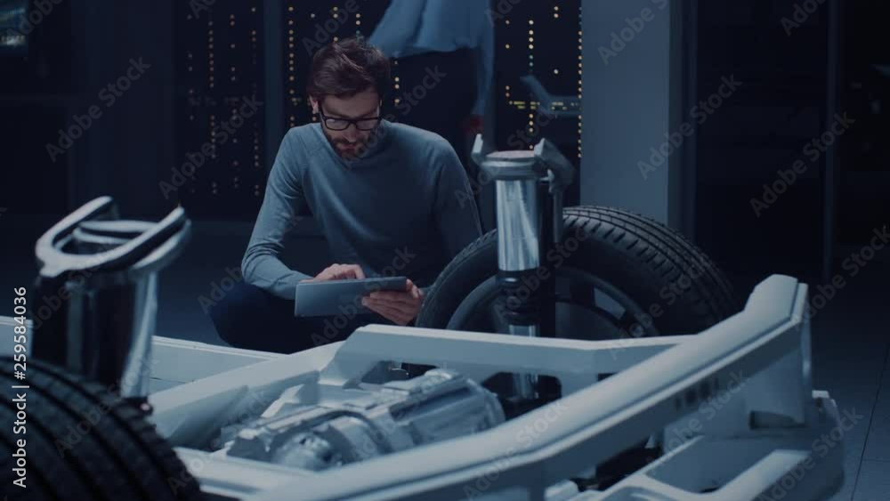 Leinwandbilder automobile design engineer sitting beside hybrid electric car chassis platform prototype, using tabl