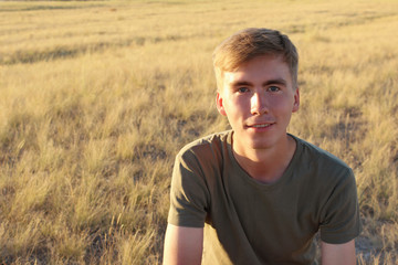 young rustic tanned guy is smiling on the background of golden grass