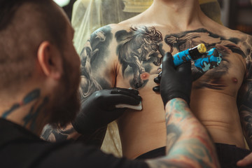 Rear view cropped shot of a professional tattoo artist wearing protective medical gloves working,...