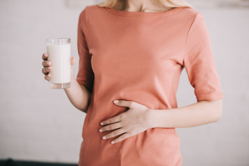 cropped view of woman holding glass of milk while having stomach ache - obrazy, fototapety, plakaty