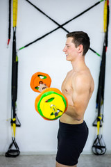 Young guy with a naked torso is engaged in barbell exercise in the gym. TRX