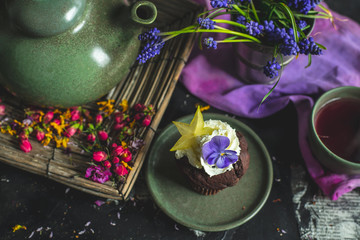 on a decorated with flower petals and flowers a dark wooden table, stands a kettle with tea, a cup...